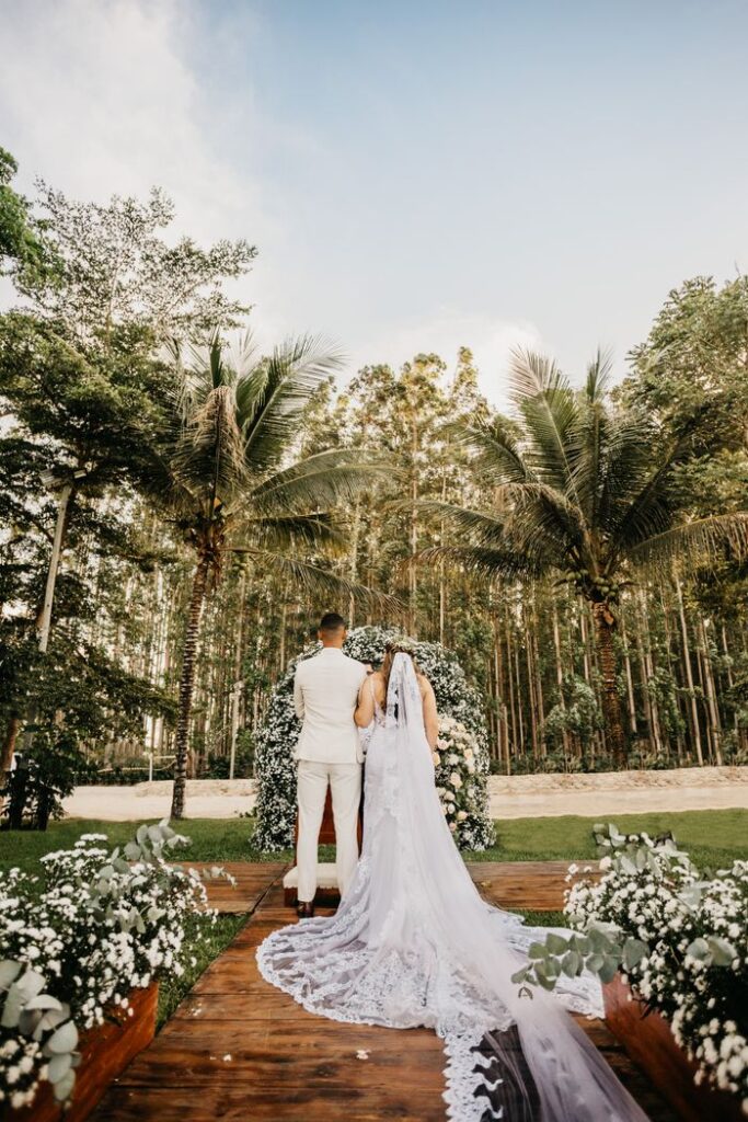 pexels photo 6544781 Back view anonymous newlywed couple wearing classy white outfits standing near arbor in lush park during solemn wedding ceremony